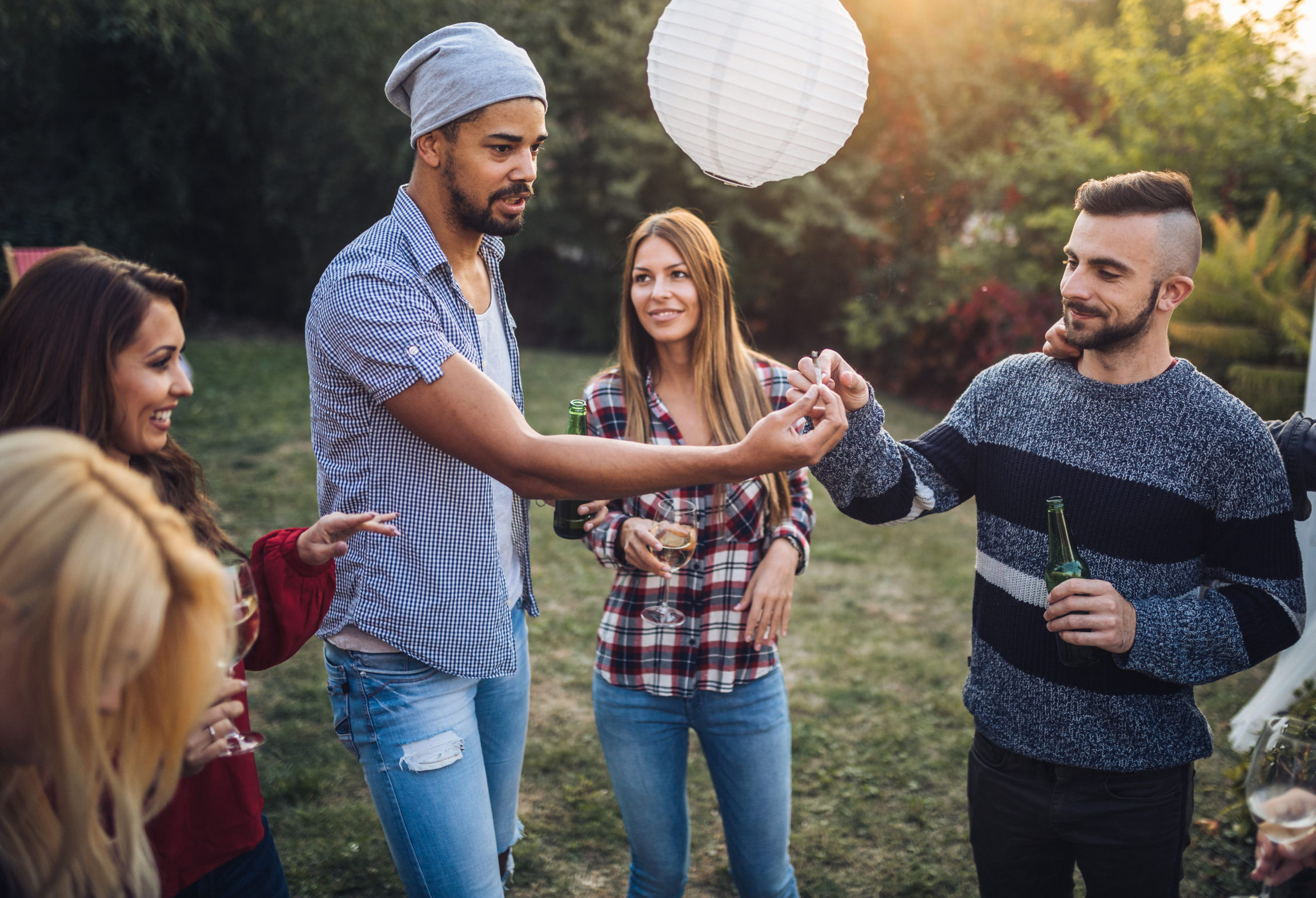 Young and mixed ethnicity group having fun together outside, drinking, and passing a joint.
