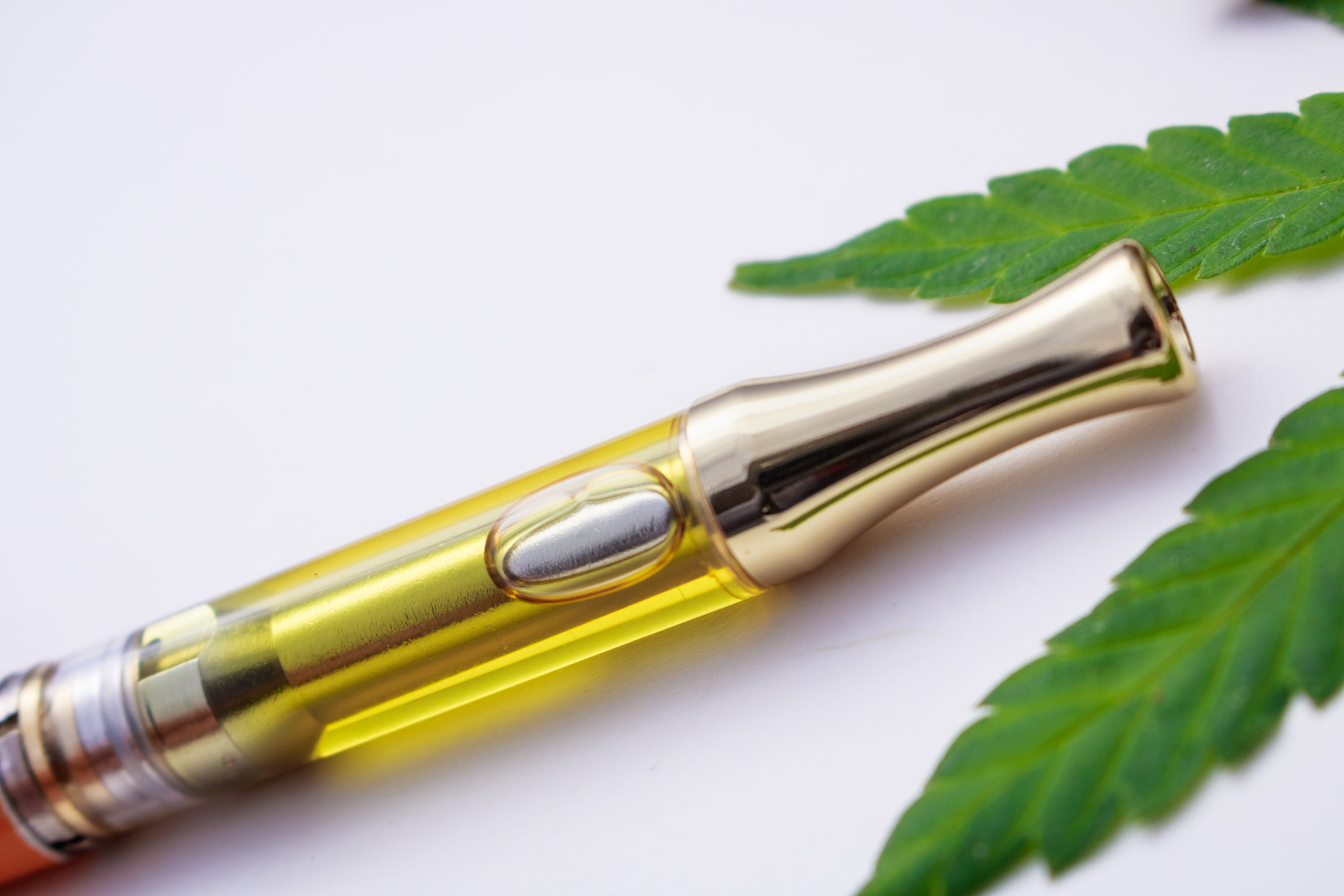 Full gram cartridge vape pen with cannabis oil and terpenes inside. Cannabis leaf on white background. 